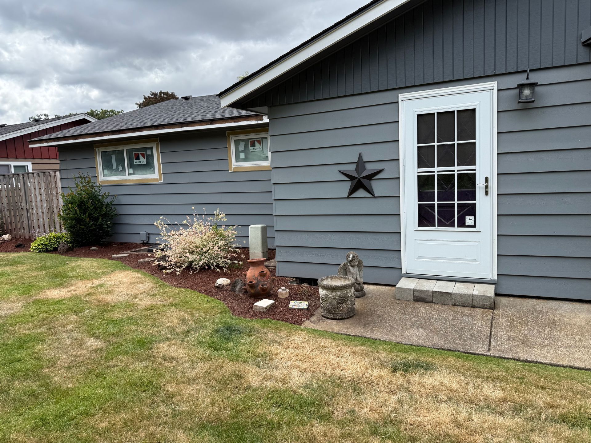 Gray house with a white door, black star, and small garden bed.