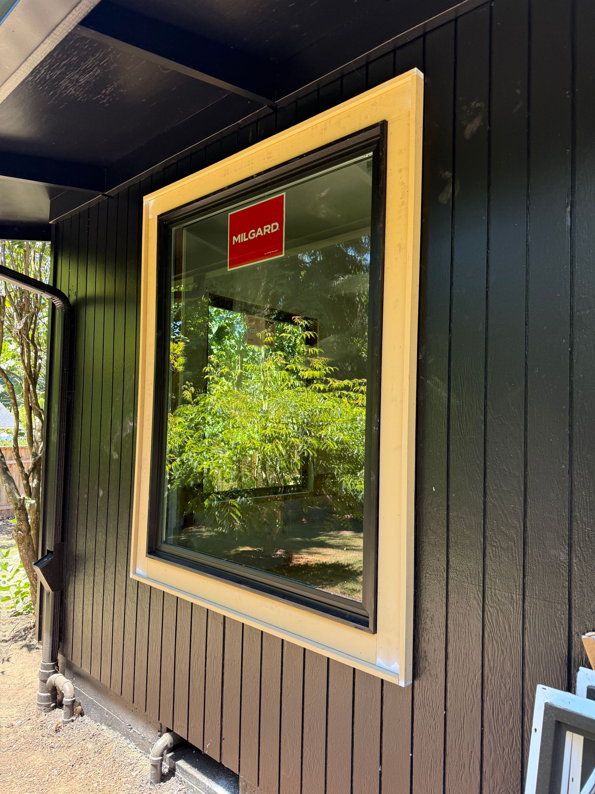 Window with a cream-colored frame and black trim; a red sign is visible inside, with a garden reflected in the glass.