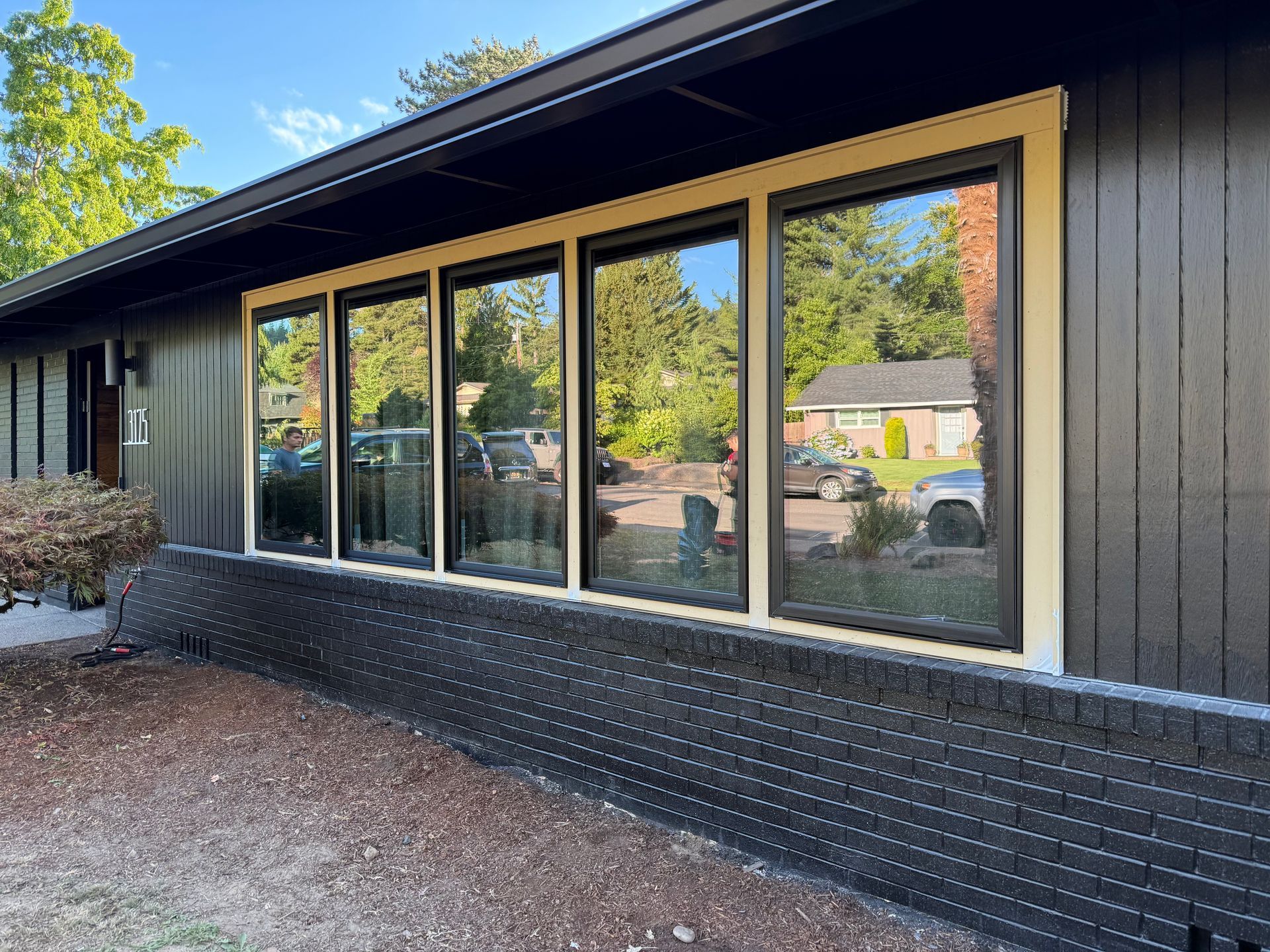 Exterior of a house with large windows, dark siding, and a black brick foundation.