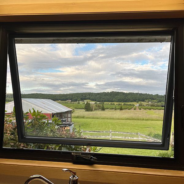 Open window with a view of a rural landscape, including a barn, fields, and a cloudy sky.