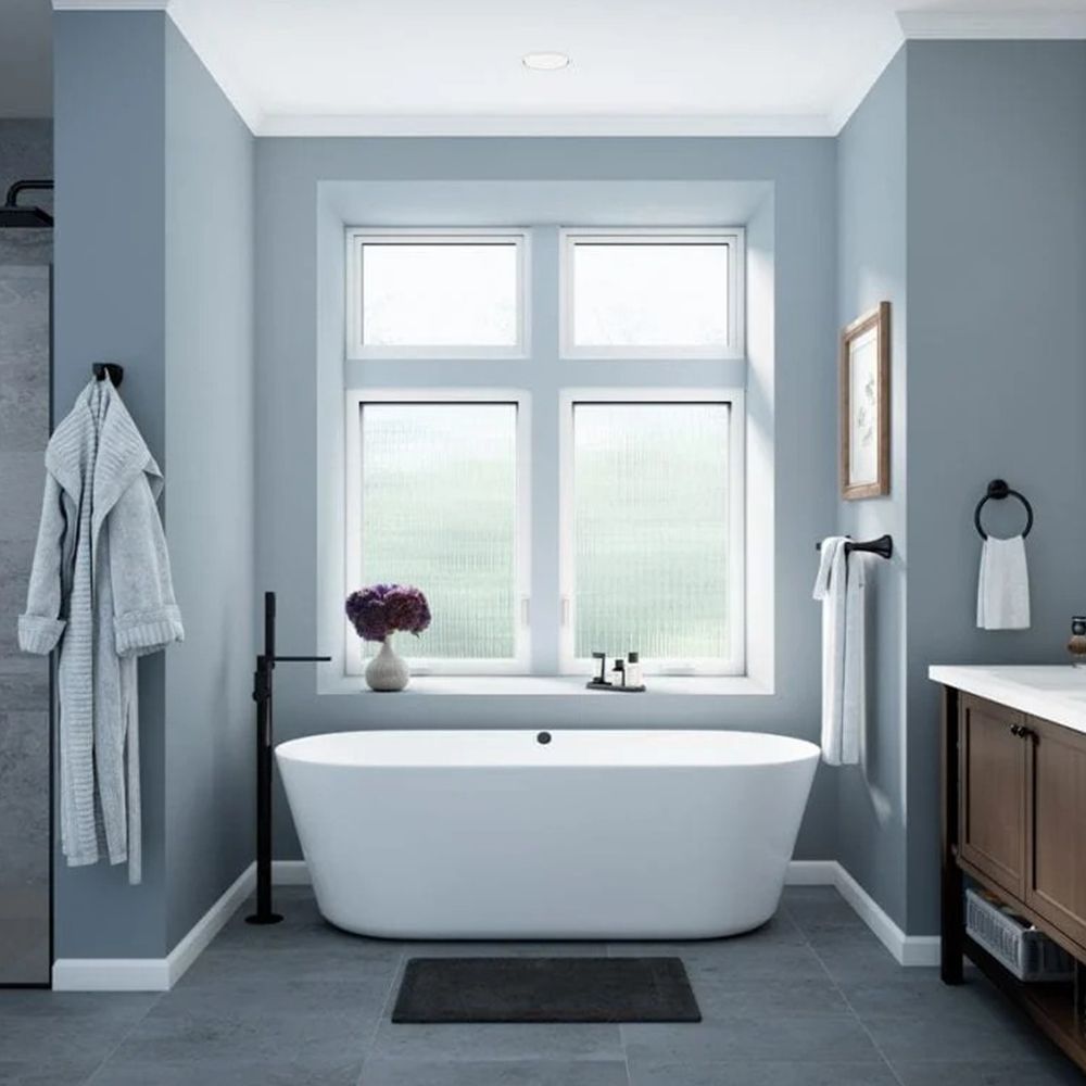 Blue bathroom with white tub in front of a window, robe hanging on the wall, and dark vanity.
