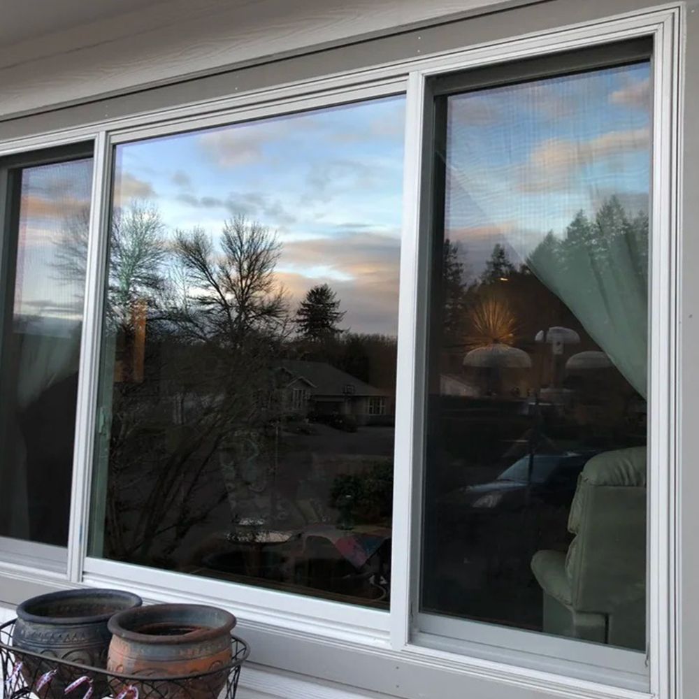 Large, three-panel window reflecting an outdoor scene: trees, sky, and a house, with pots on the sill.