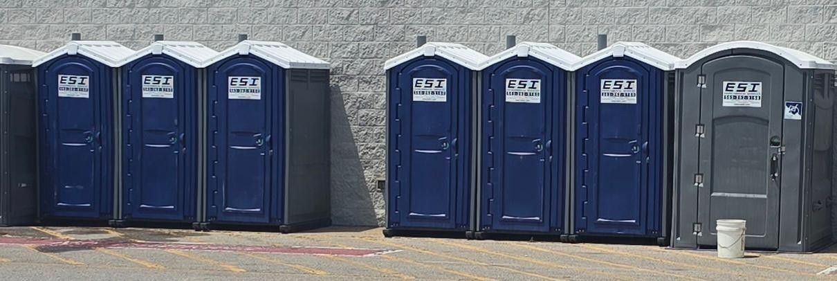 Portable blue and gray toilet stalls lined up against a wall.