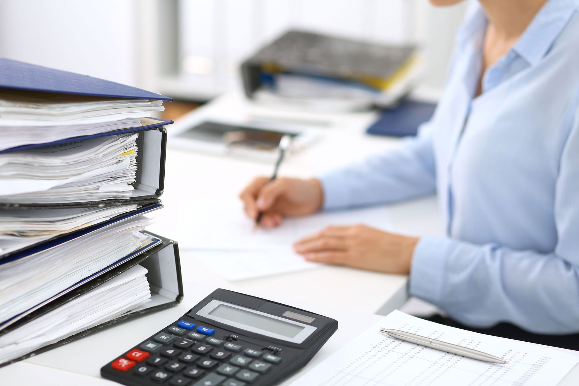 A woman is sitting at a desk with a calculator and a pen.