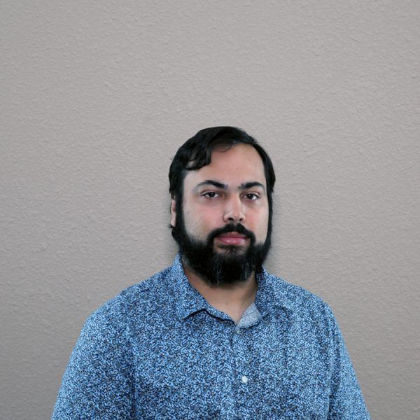 A man with a beard wearing a blue shirt is standing in front of a wall.