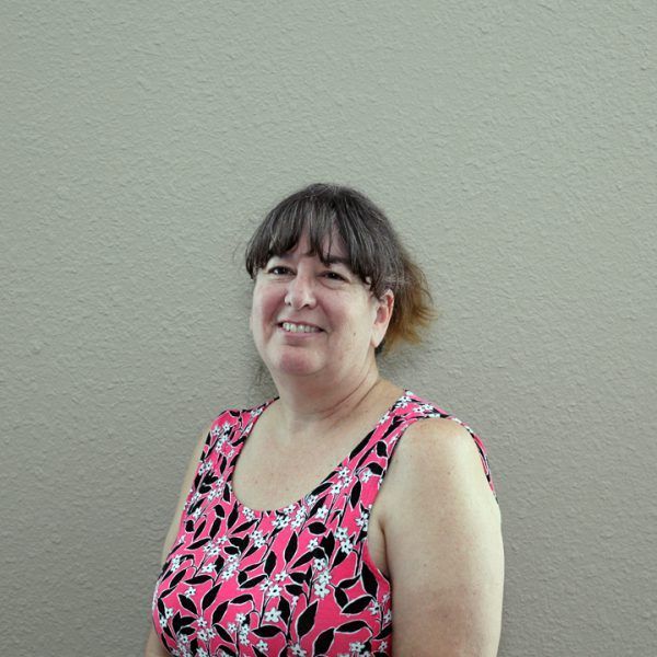 A woman in a pink floral tank top is smiling for the camera