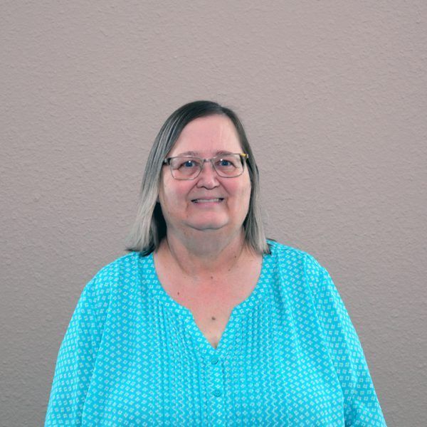 A woman wearing glasses and a blue shirt is smiling for the camera.