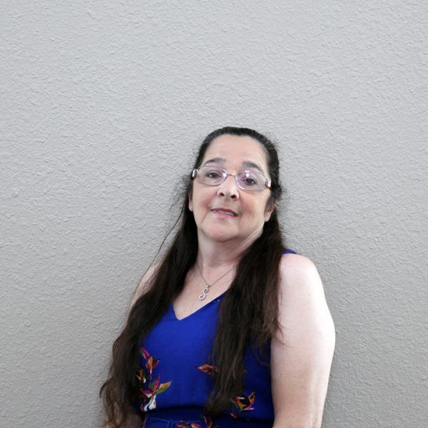 A woman wearing glasses and a blue dress is standing in front of a wall.