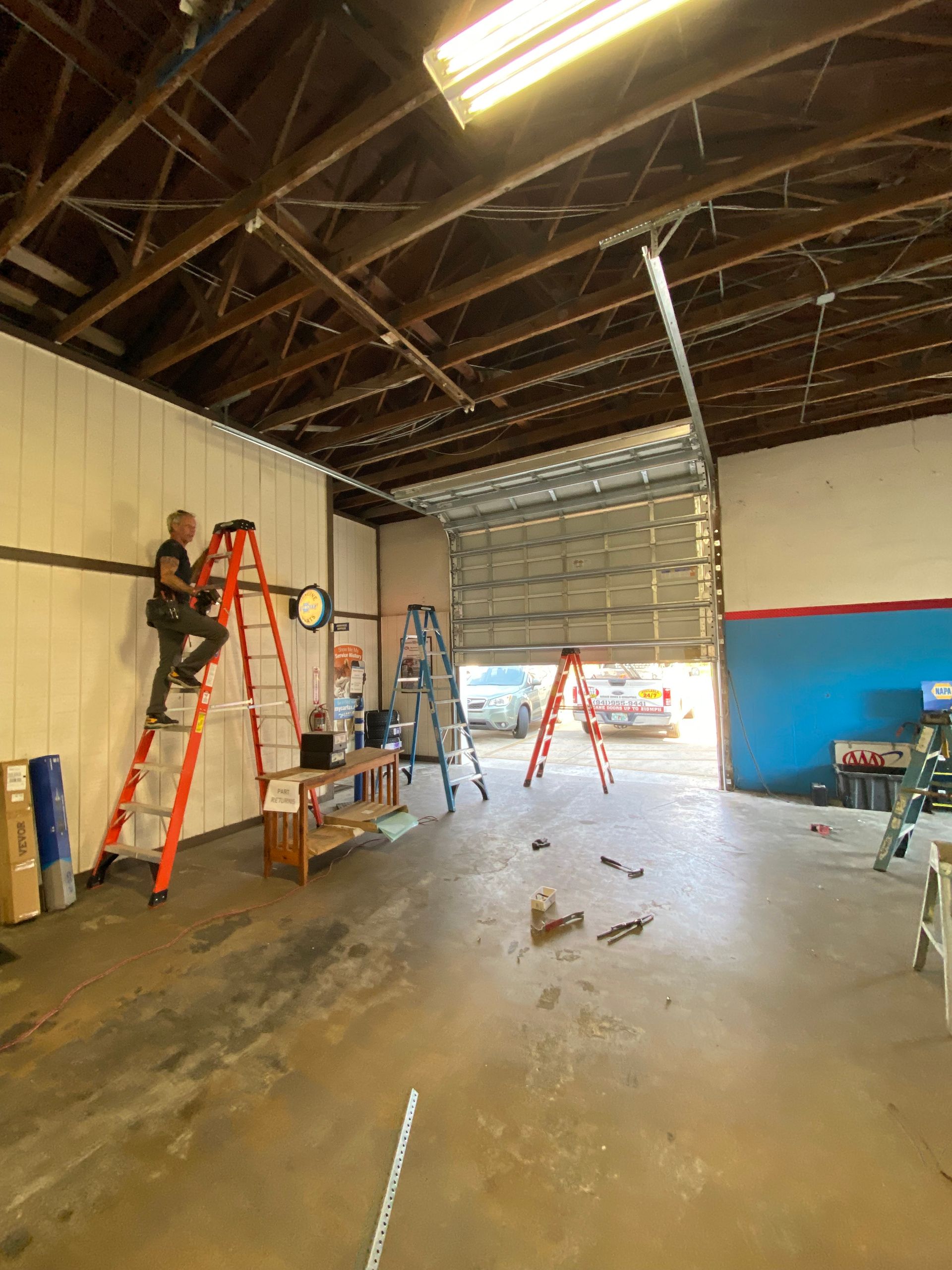 A man is sitting on a ladder in a garage working on a garage door.