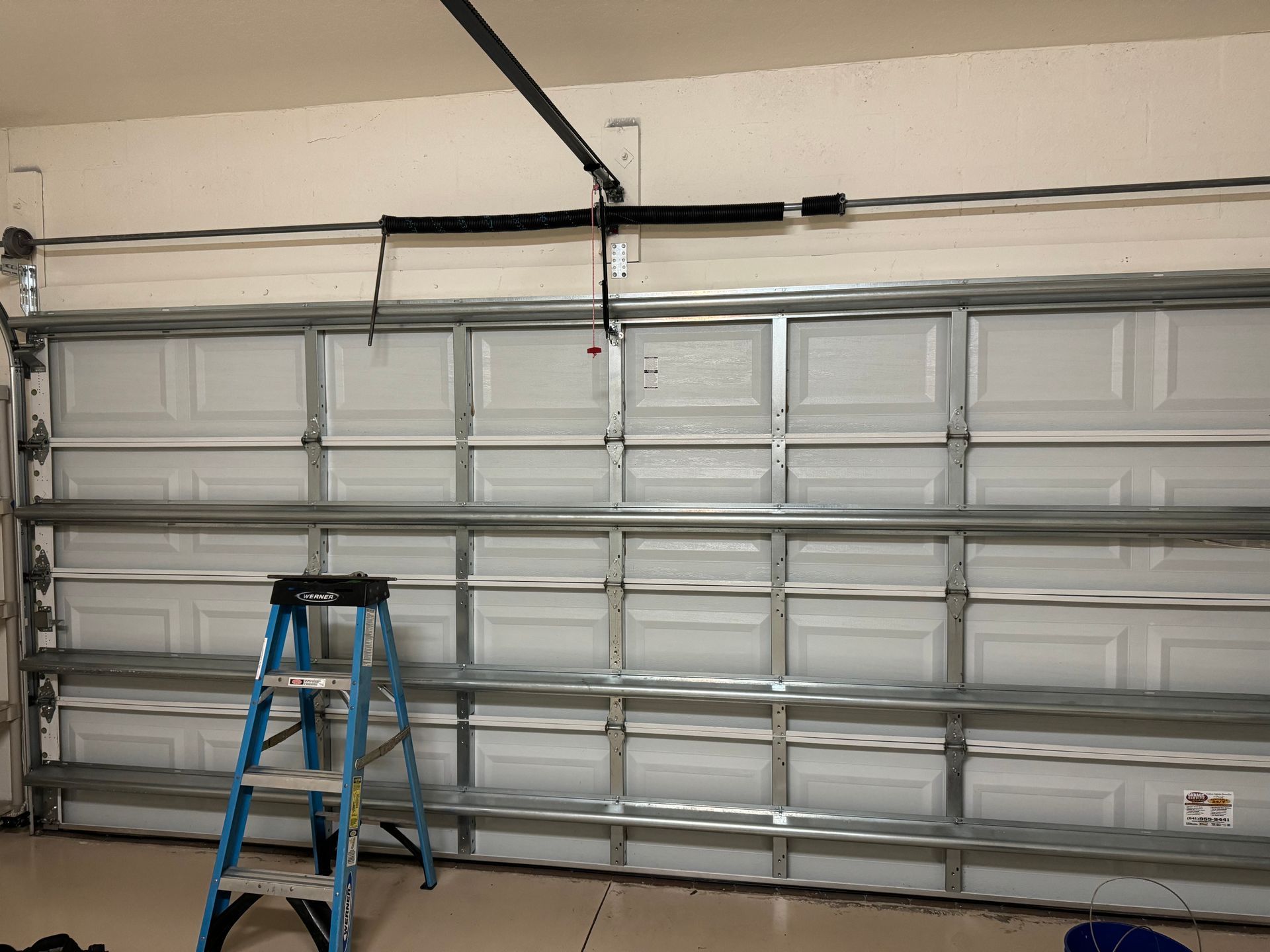 A blue ladder is sitting in front of a garage door.