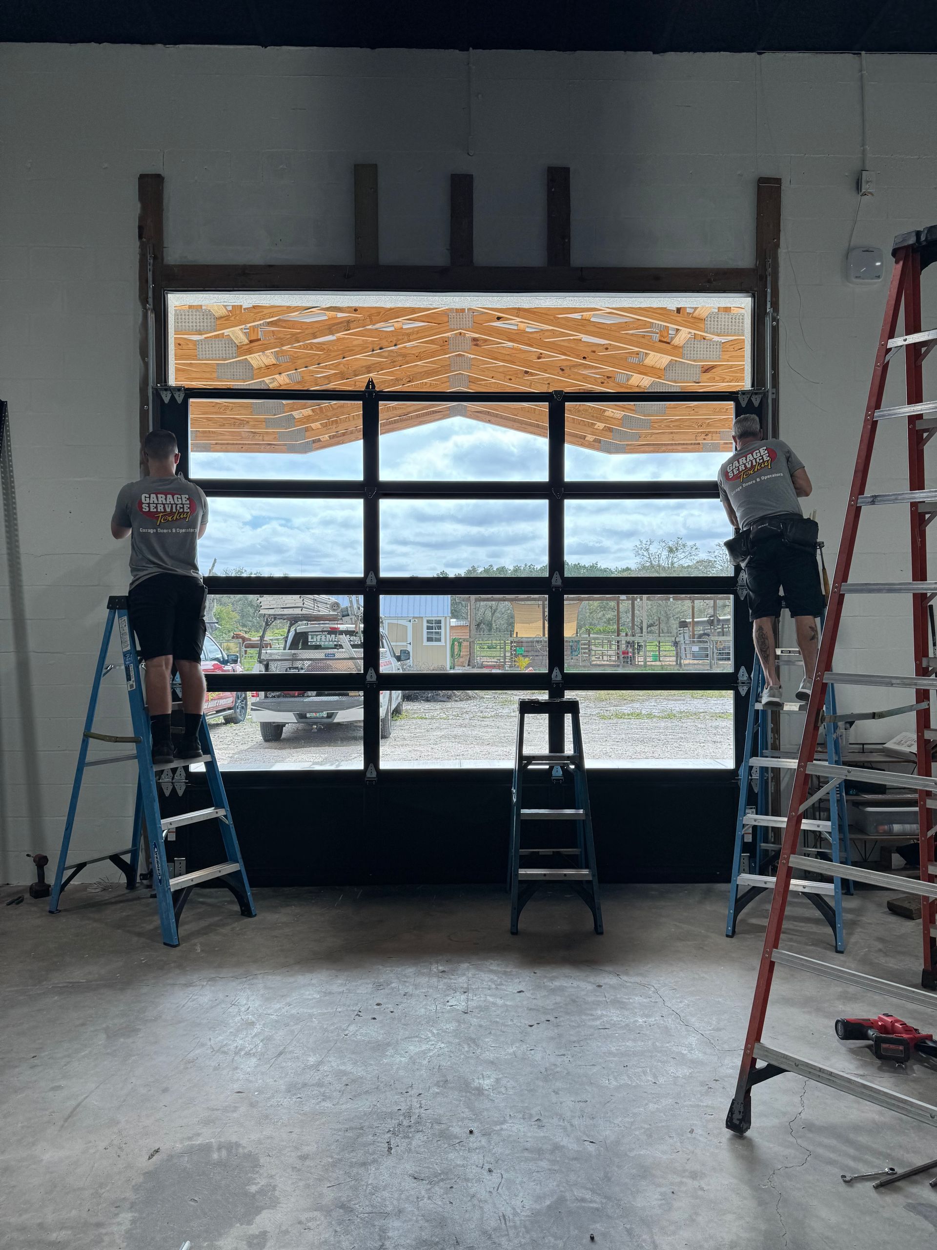 Two men are standing on ladders in front of a garage door.