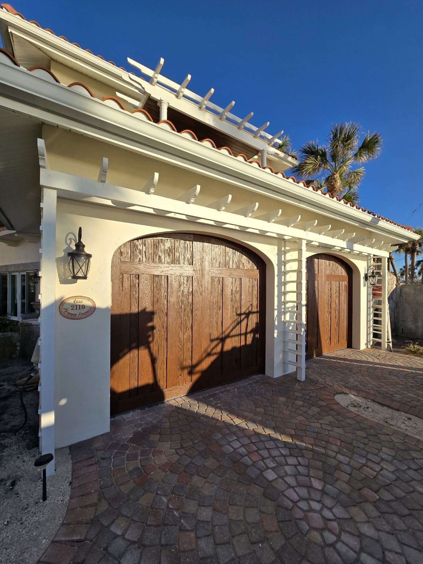 A white house with two wooden garage doors and a brick driveway.