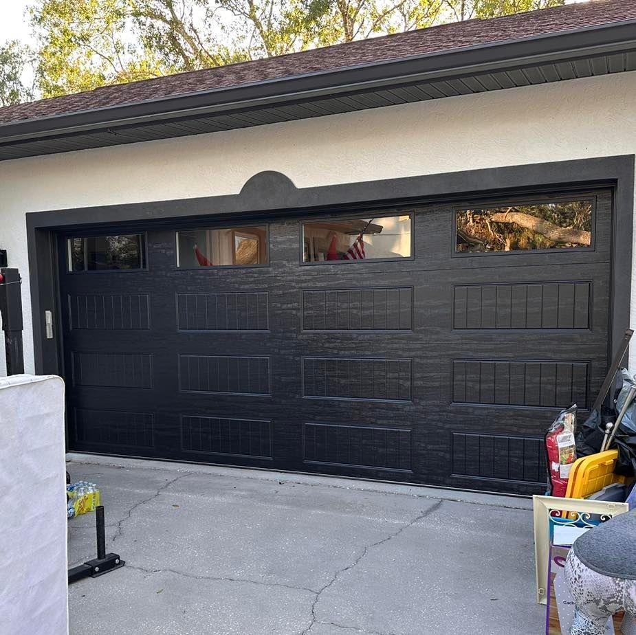 A black garage door is sitting in front of a white house.