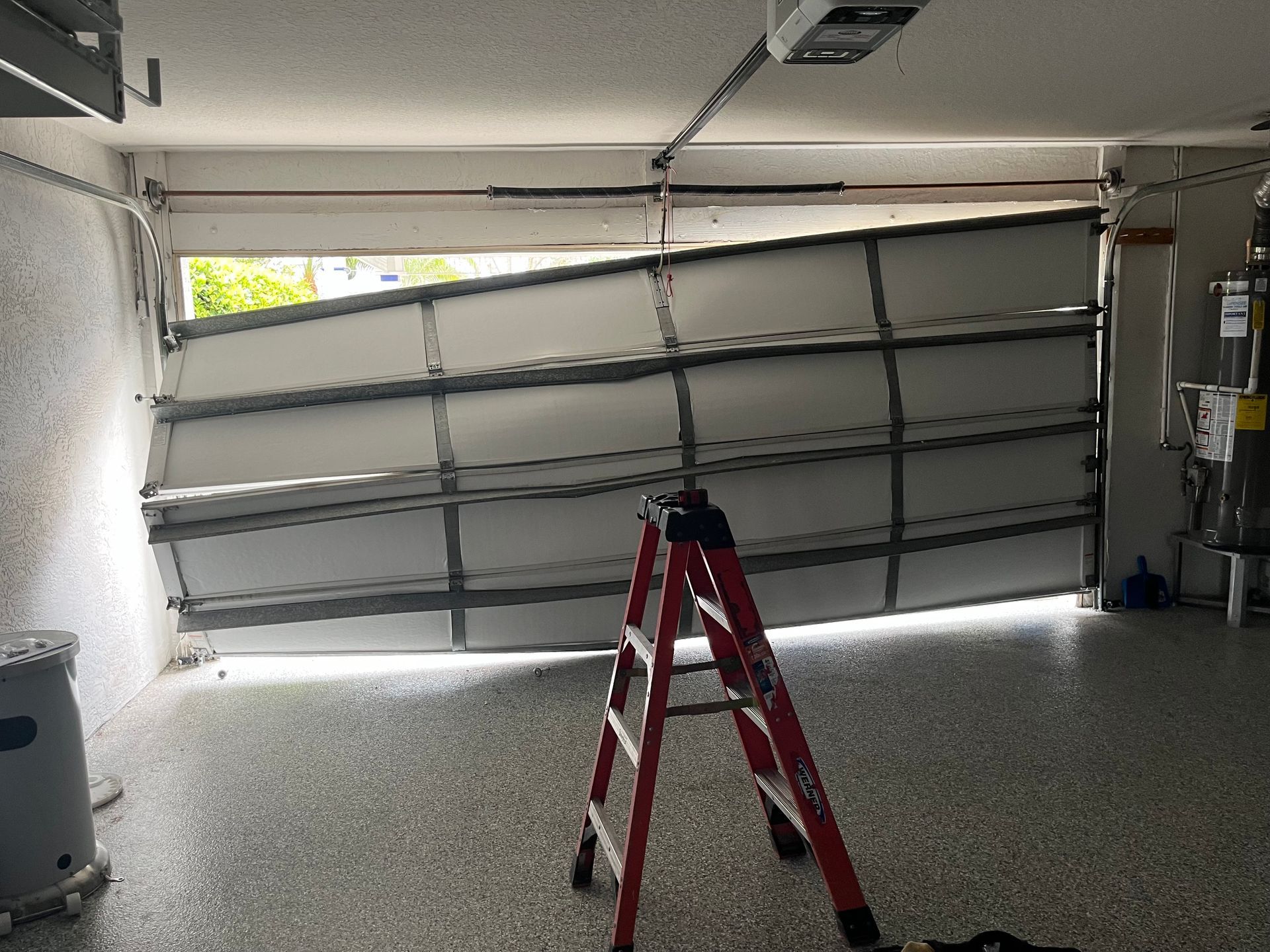 A red ladder is sitting in front of a broken garage door.