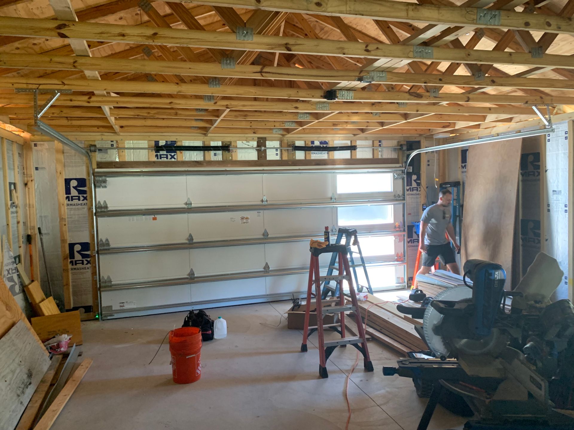 A man is working on a garage door in a building under construction.