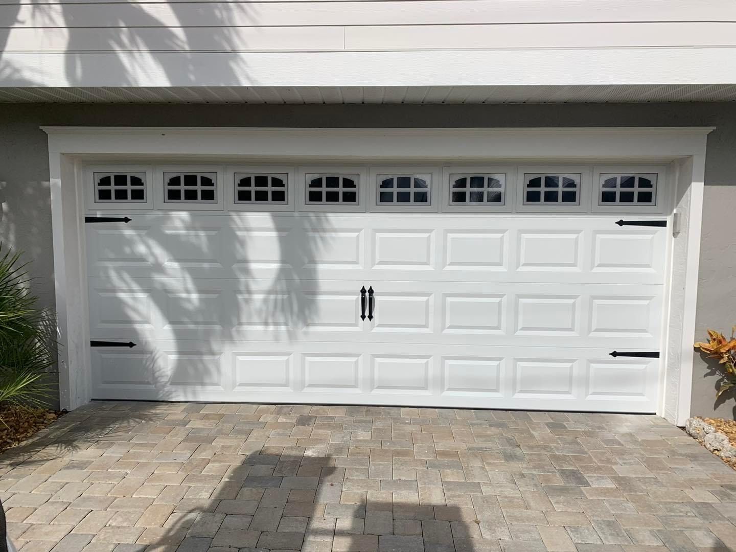 A white garage door with black handles is sitting on a brick driveway.