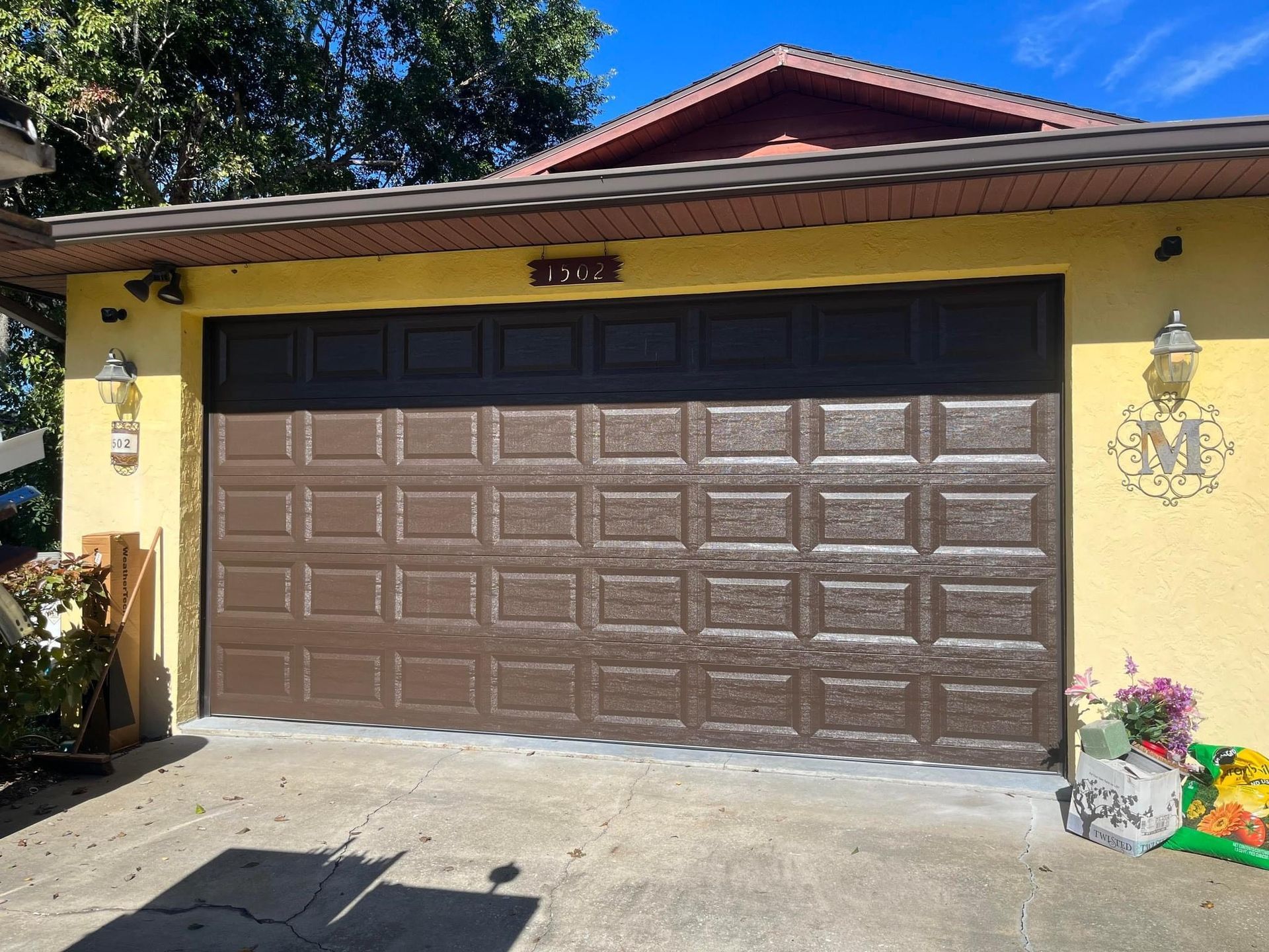 A large brown garage door is sitting in front of a yellow house.