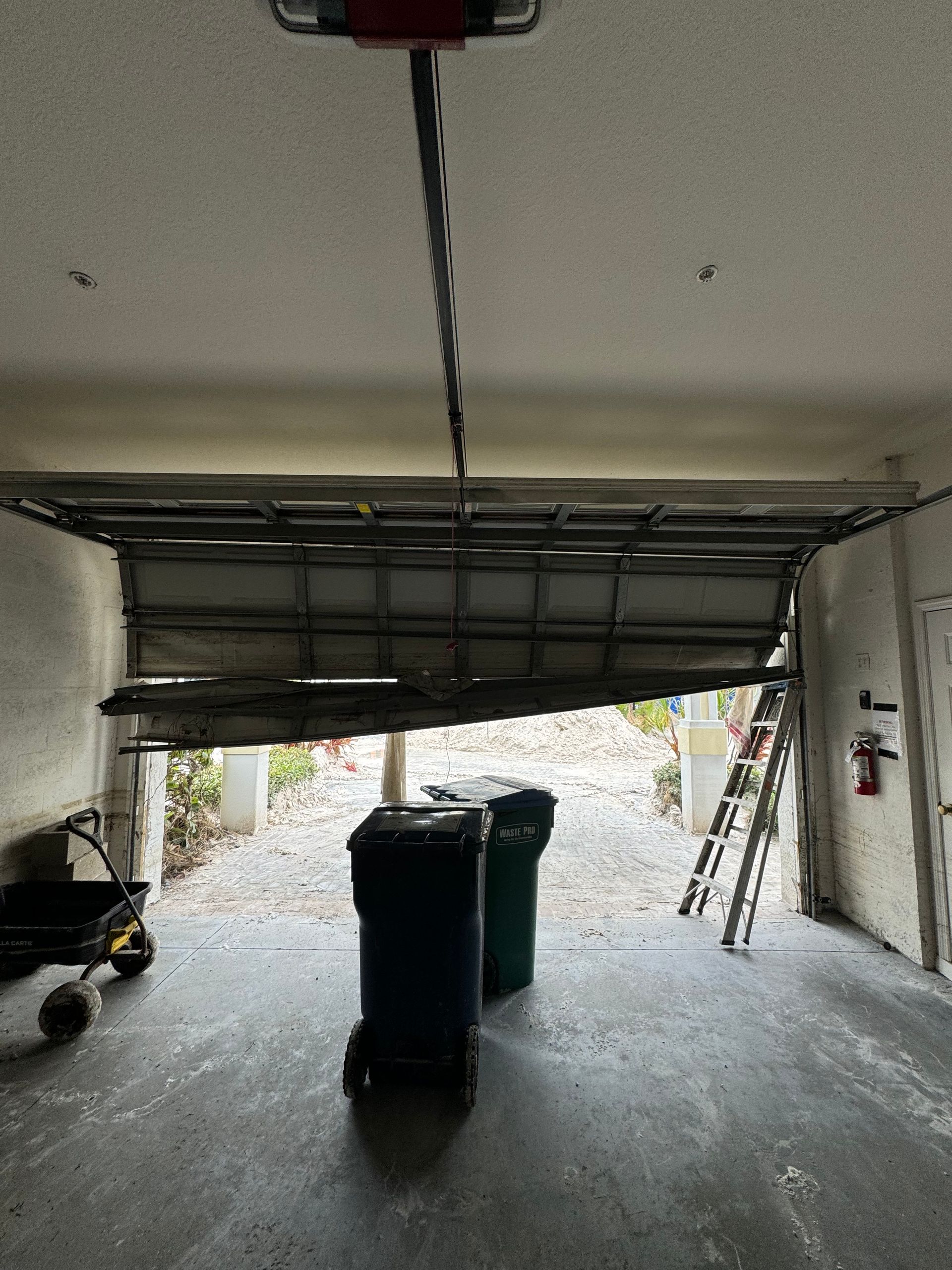 A garage with a broken garage door and trash cans in it.
