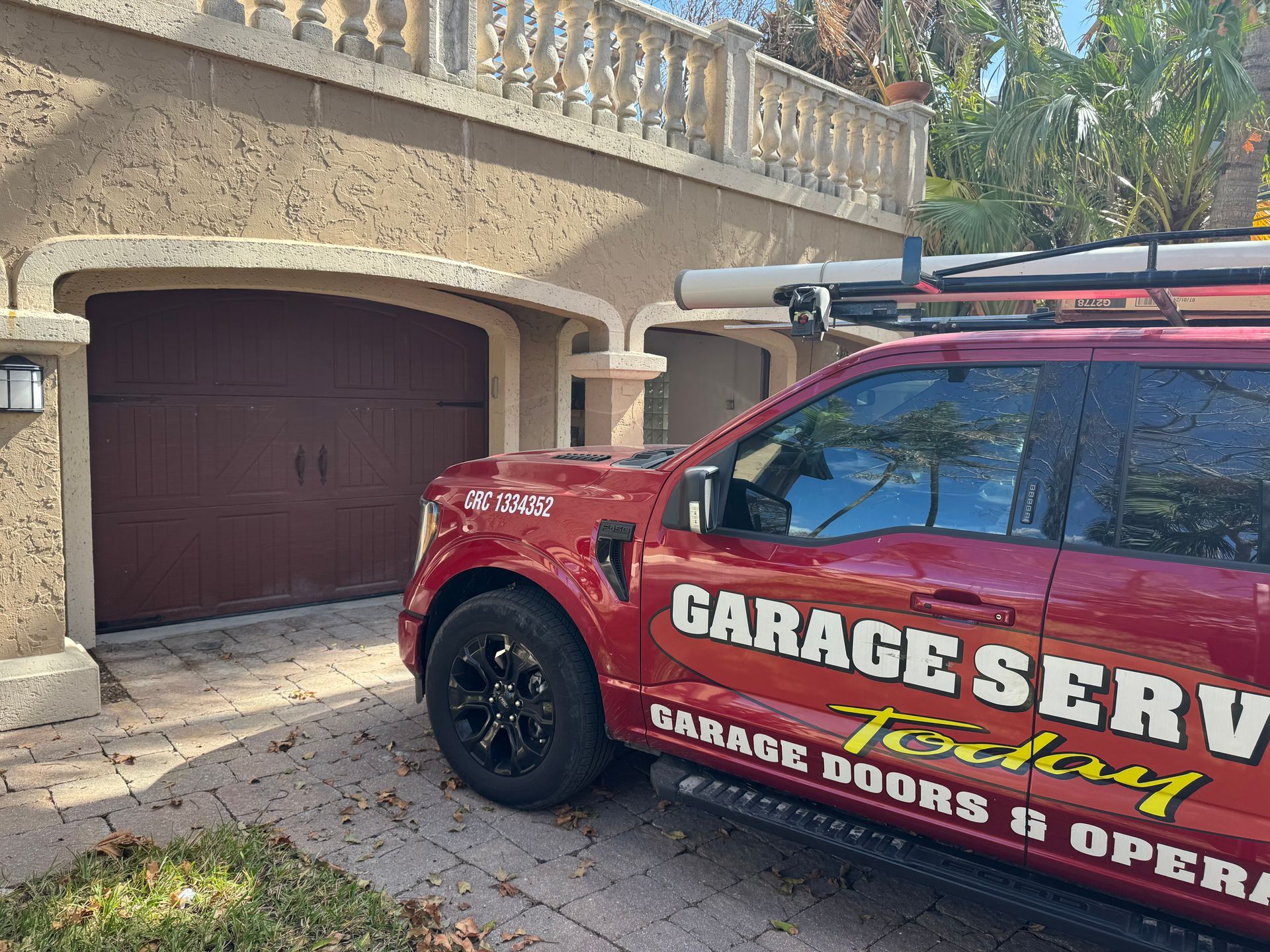 A red garage service truck is parked in front of a garage door.