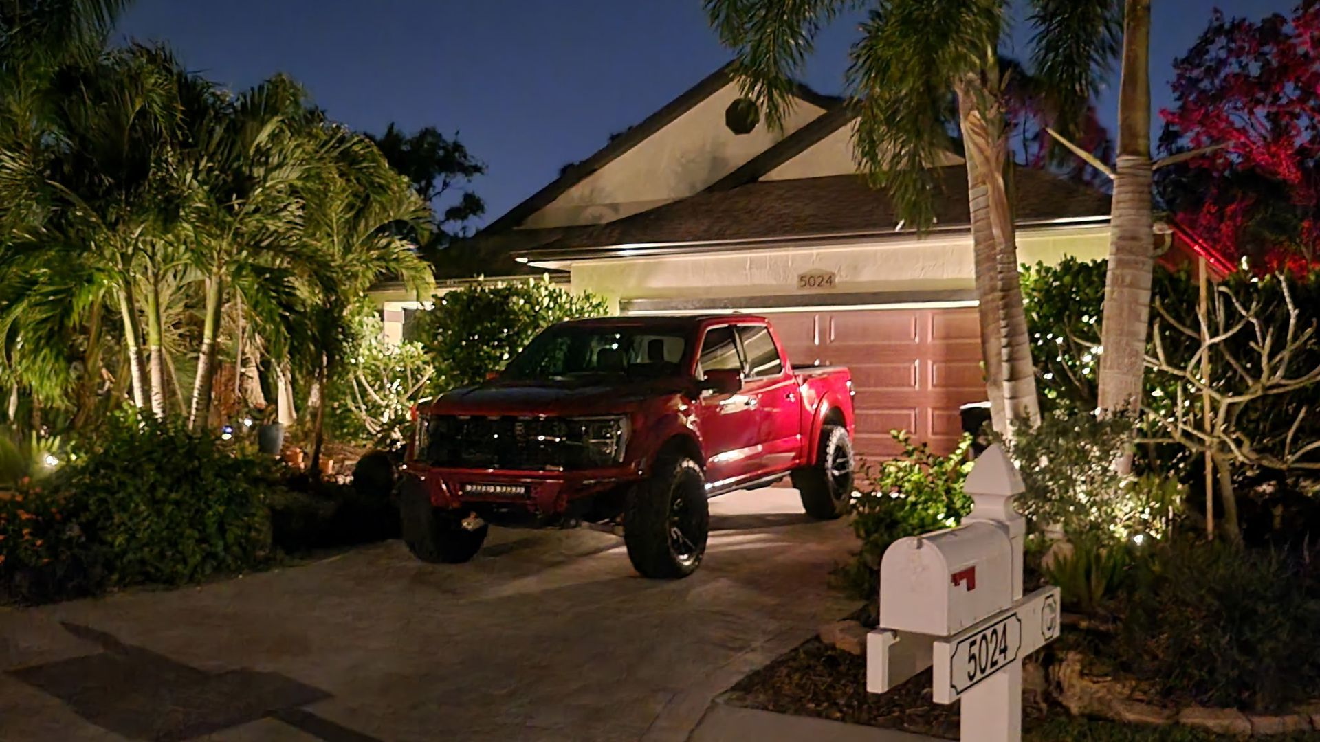 A red truck is parked in front of a house at night.
