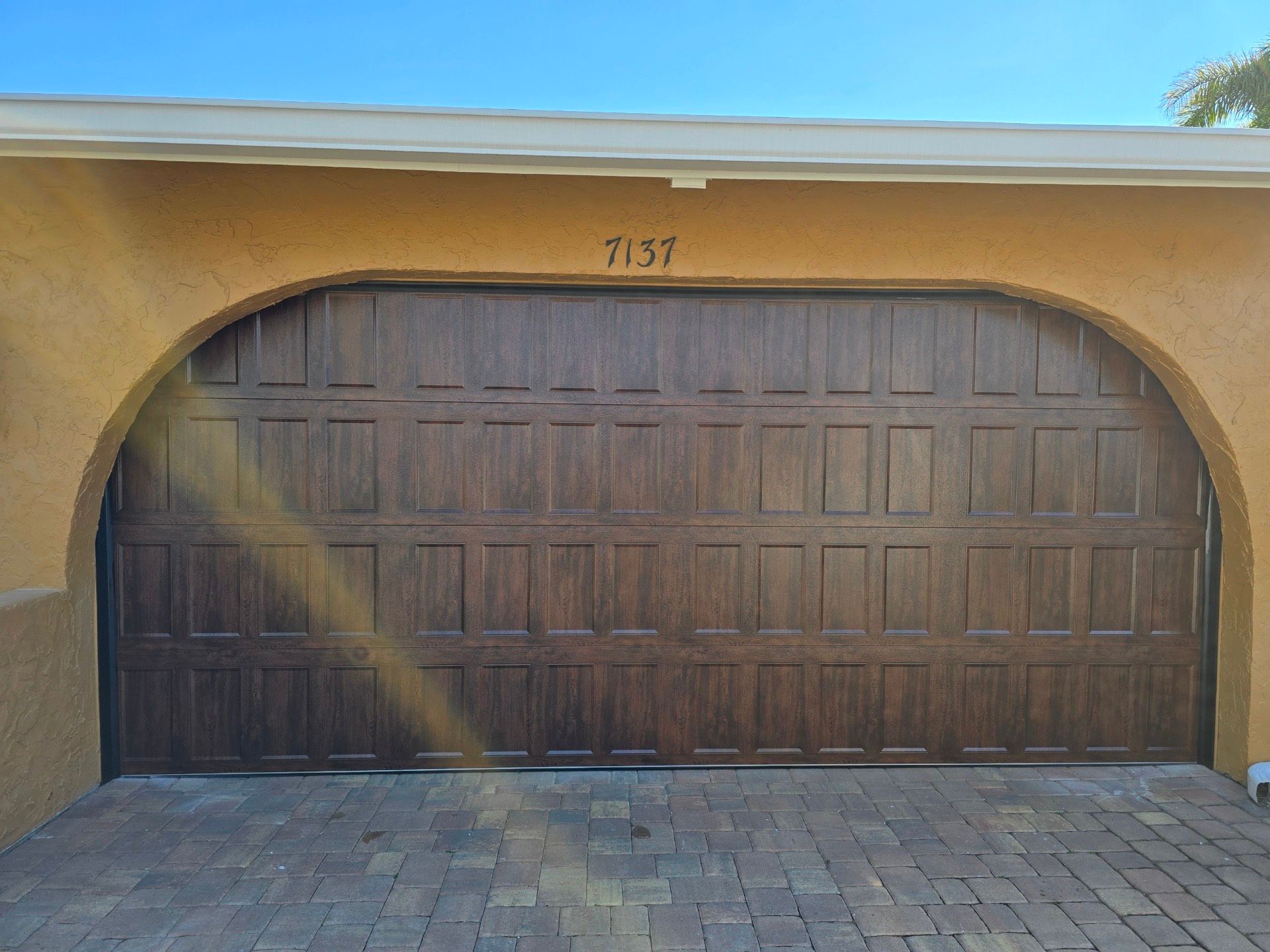 A large wooden garage door is sitting on top of a brick driveway.