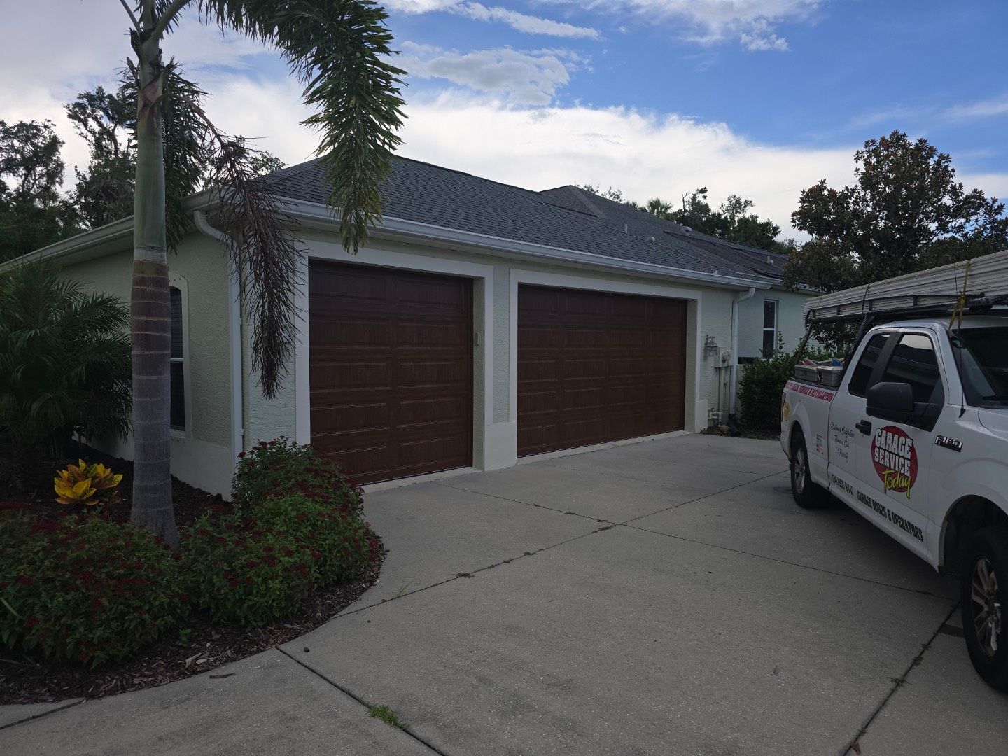 A white truck is parked in front of a house with two garage doors.