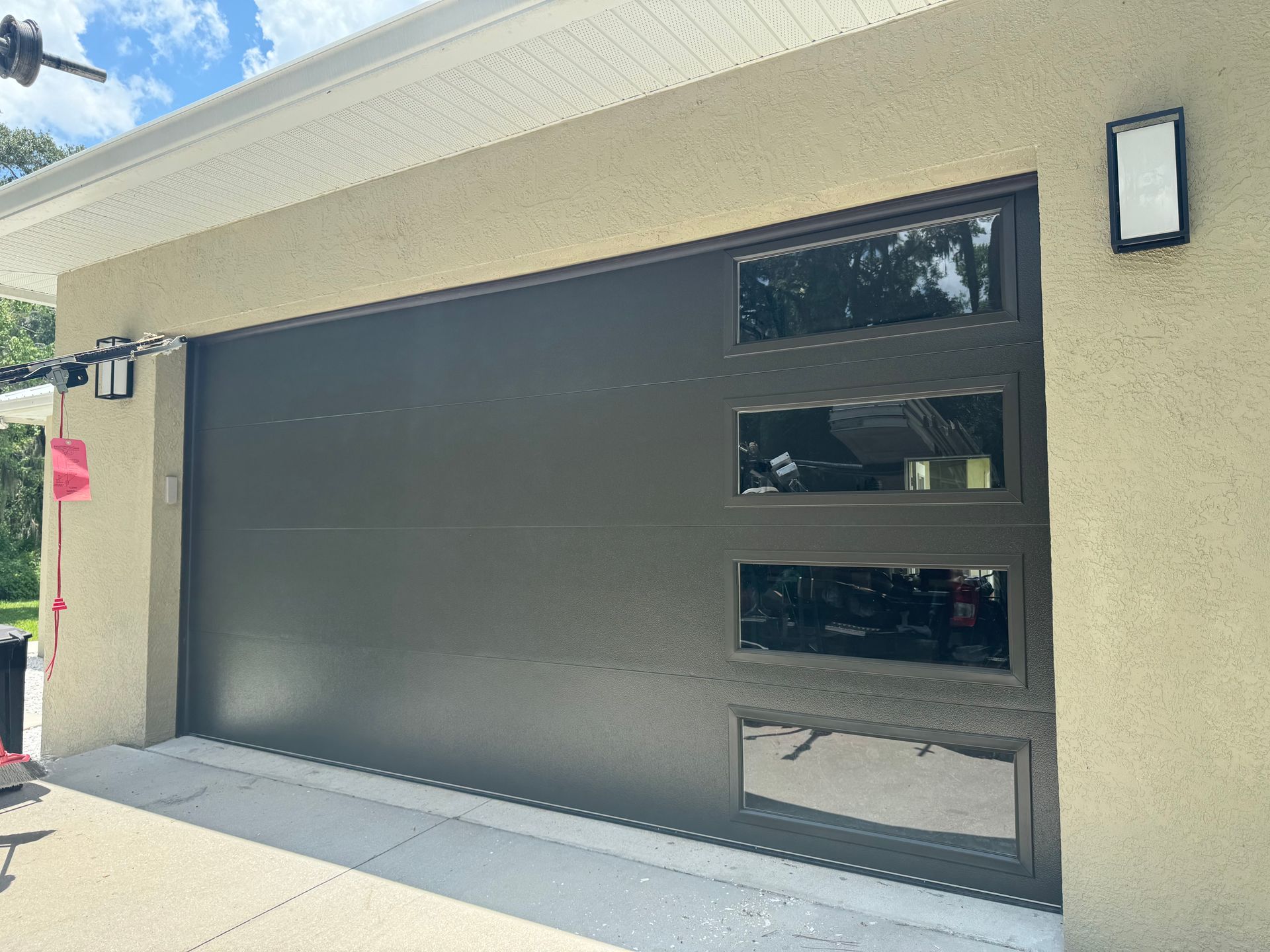 Black modern garage door with three narrow windows on a stucco house exterior.