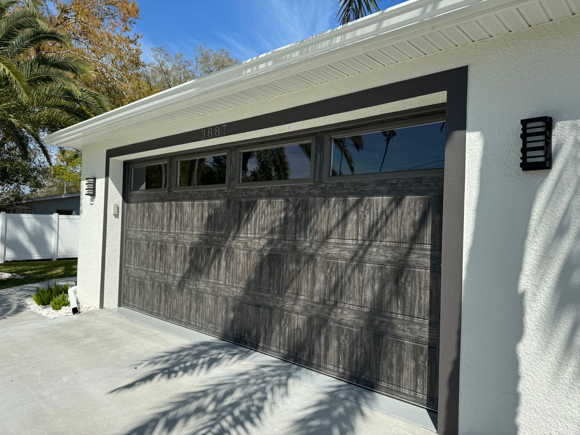 Modern white house garage with a dark wood door and narrow window panels under bright sunlight.