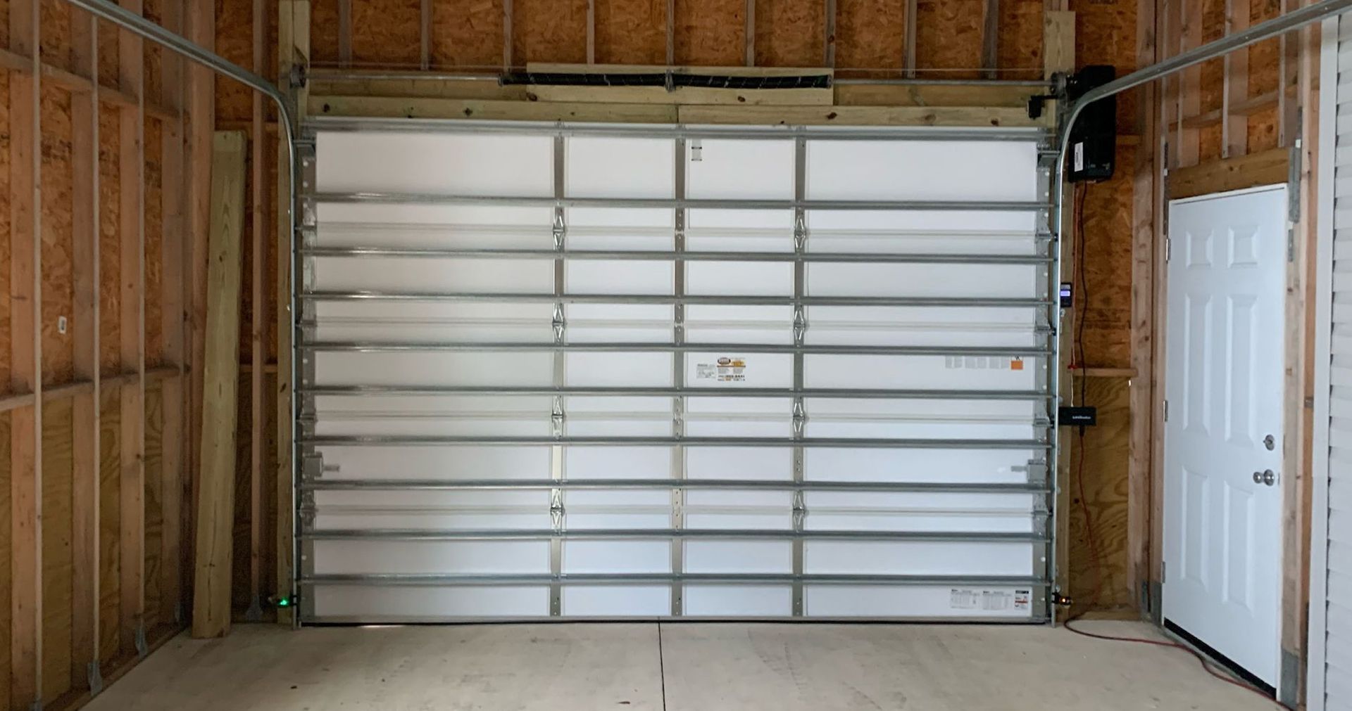 Empty garage interior with white roll-up door and exposed wooden framing.