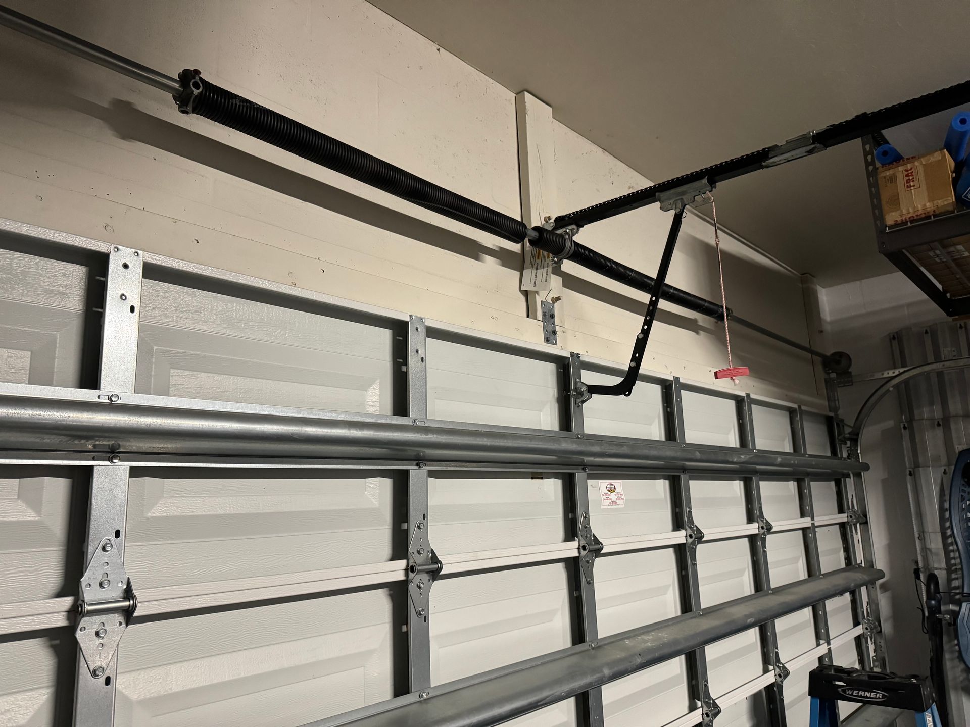 Garage with a white sectional door, black track hardware, and exposed ceiling pipes.