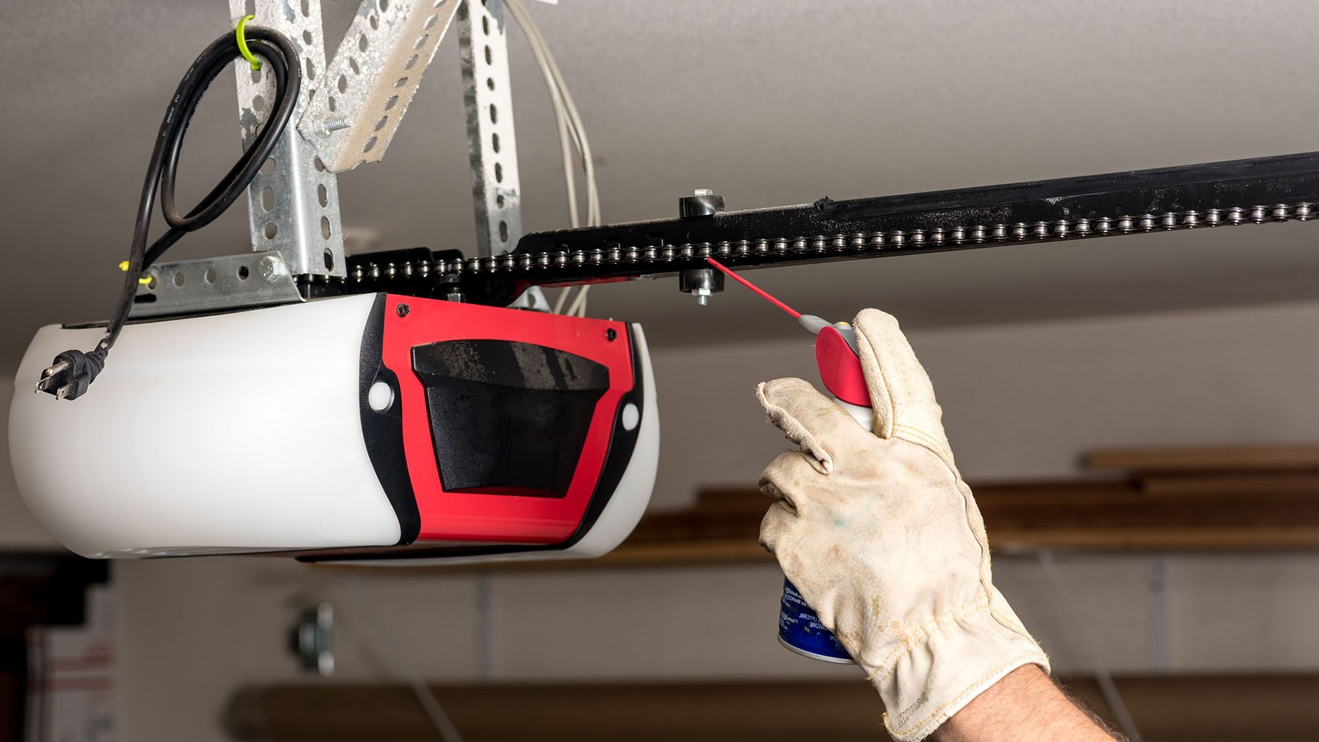 Person in gloves inspecting a white garage door opener with a red panel and black rail.
