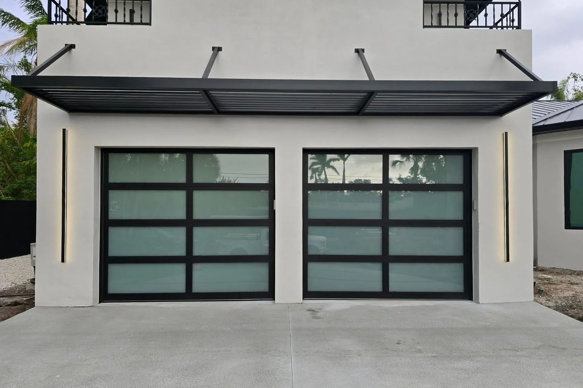 Modern two-car garage with frosted glass doors and a black awning on a white house exterior.