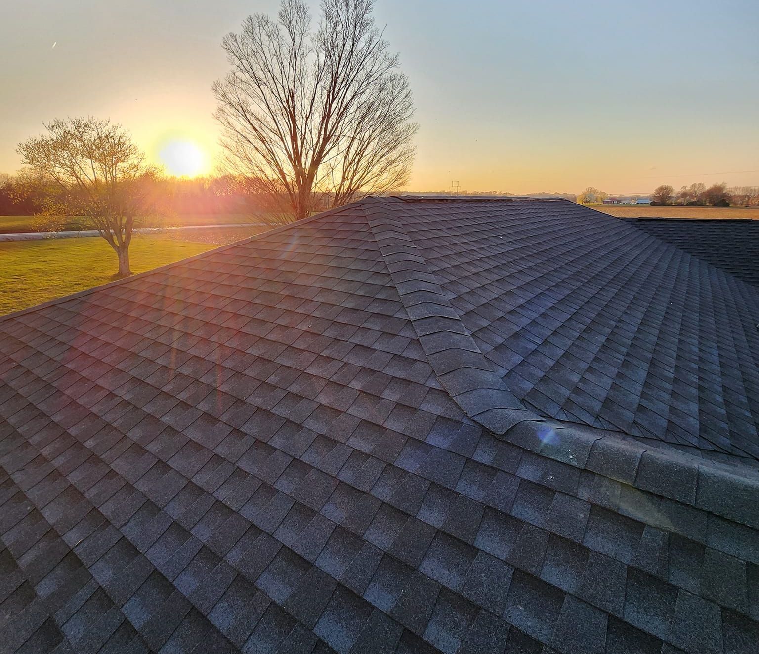 The sun is setting behind the roof of a house.