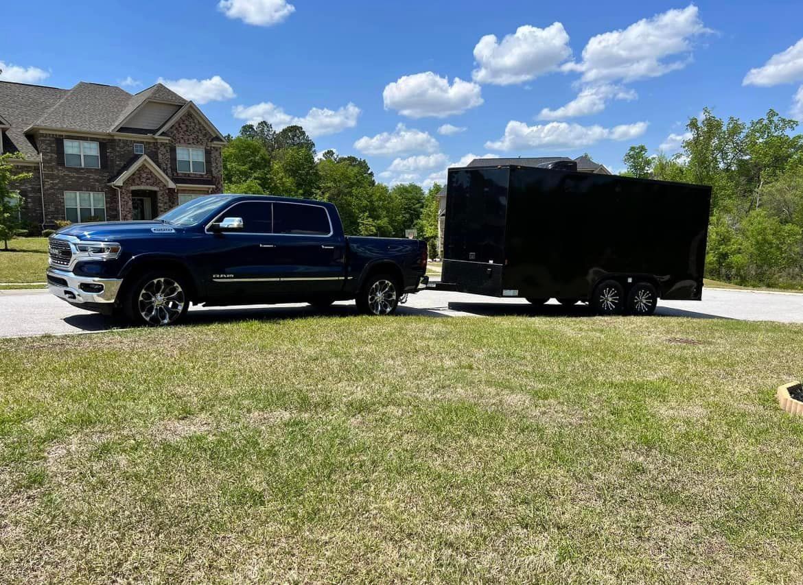 A blue truck is towing a black trailer in front of a house.