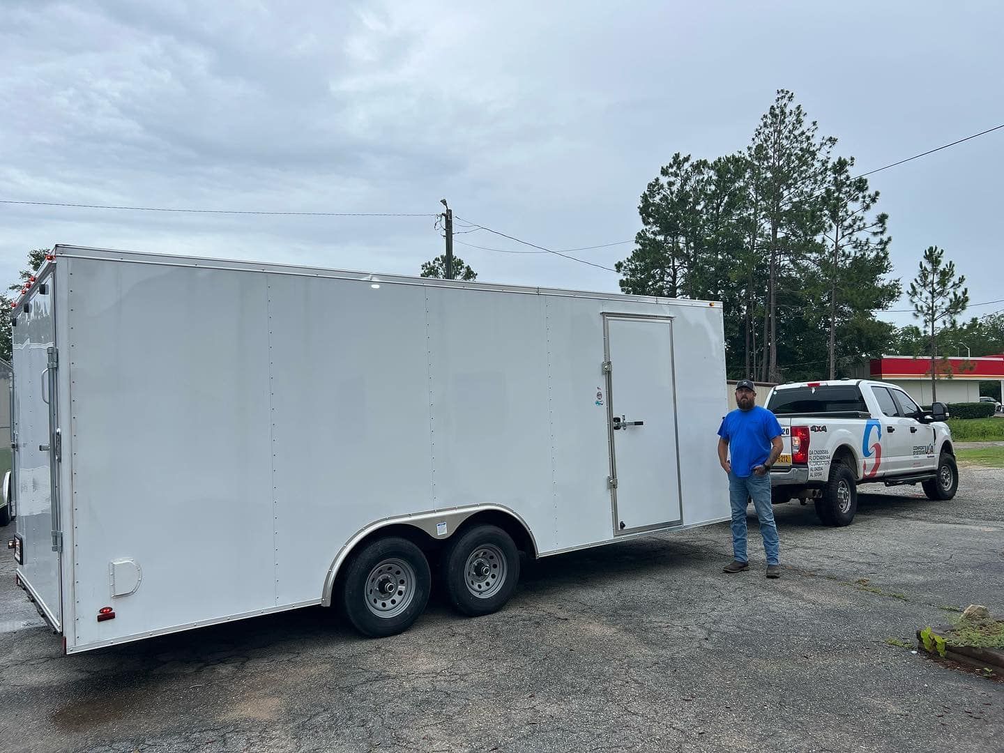 A man is standing next to a white trailer in a parking lot.