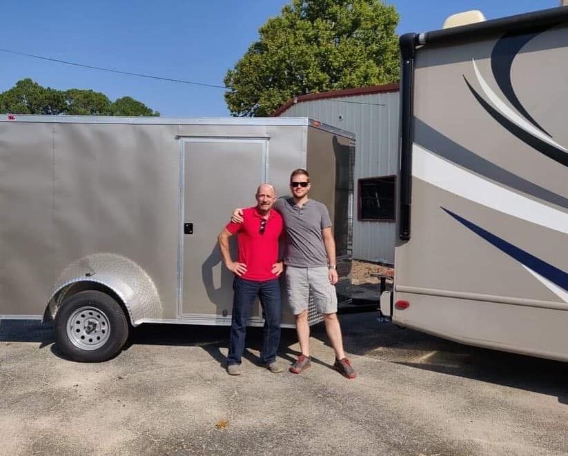 Two men standing next to a trailer and a rv