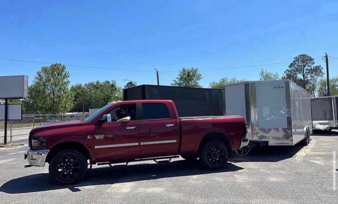 A red truck is towing a trailer in a parking lot.