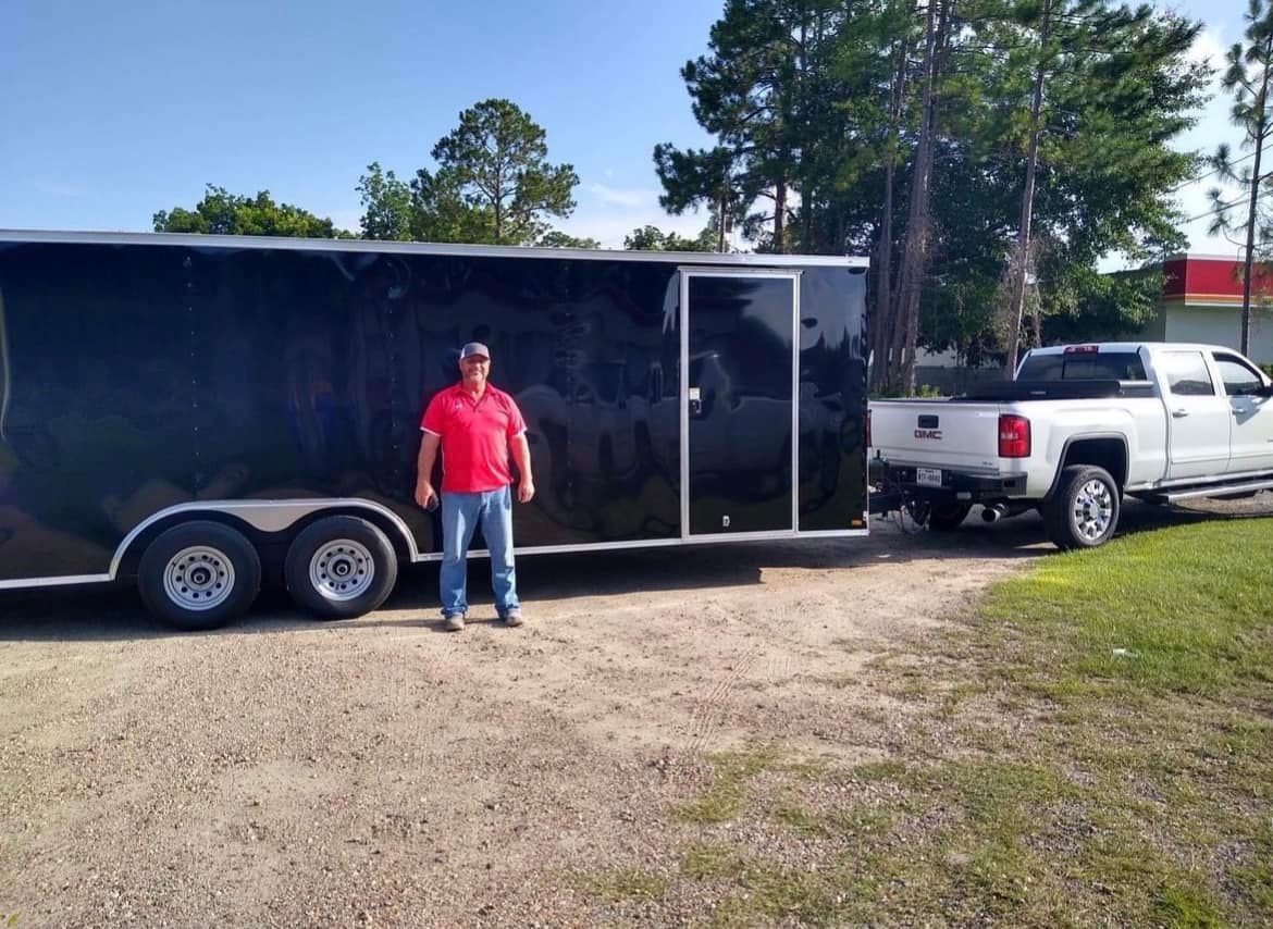 A man is standing in front of a trailer and a truck.