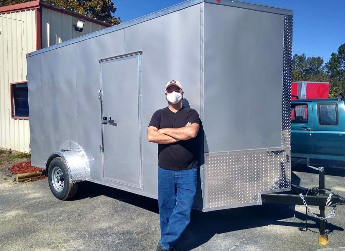 A man wearing a mask is standing in front of a trailer.