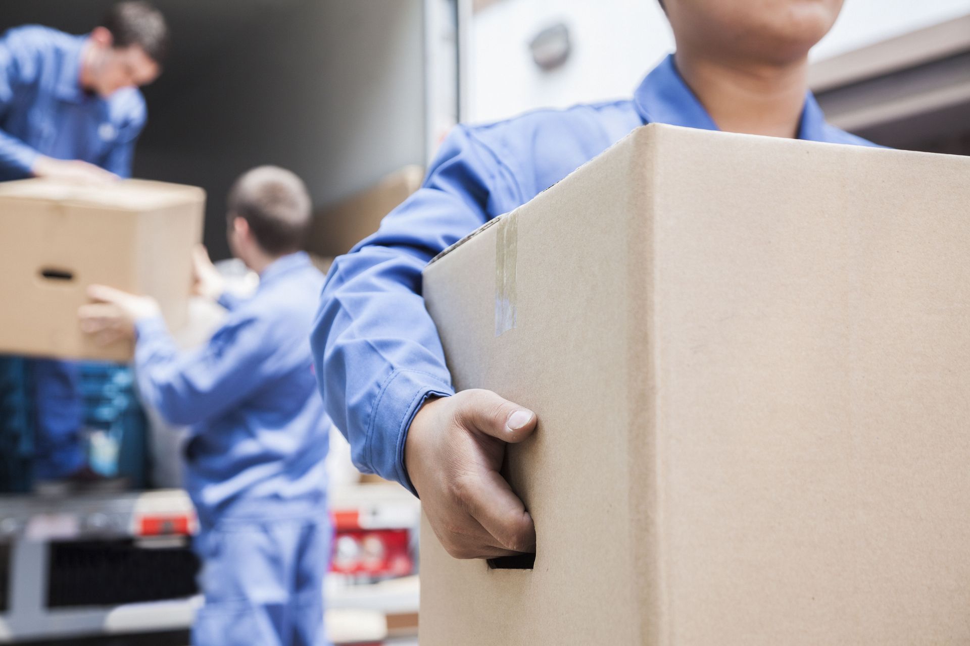 Warehouse workers in blue uniforms carrying cardboard boxes in a busy storage area
