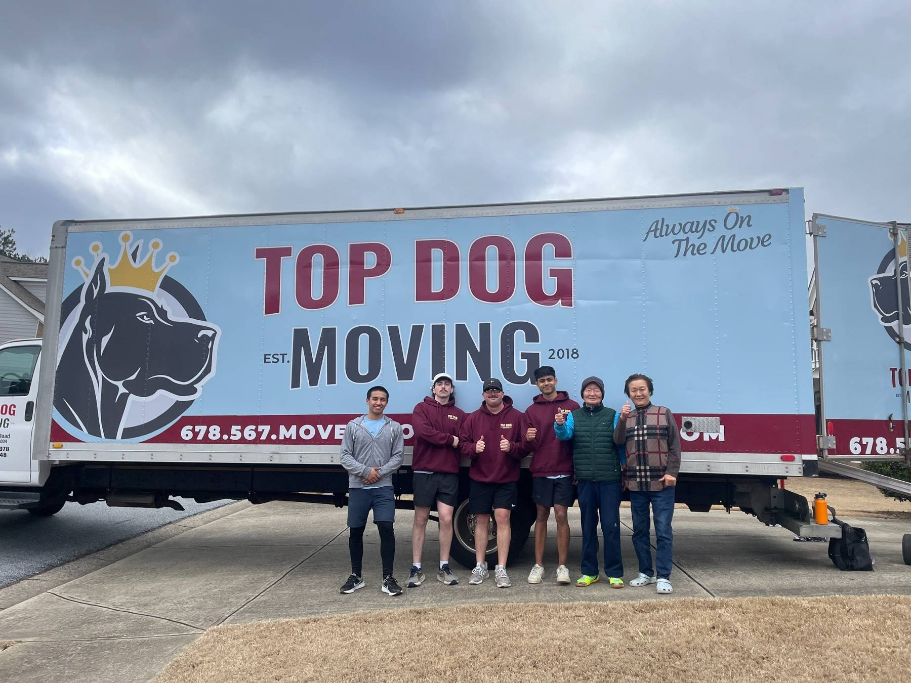 A group of people standing in front of a top dog moving truck.