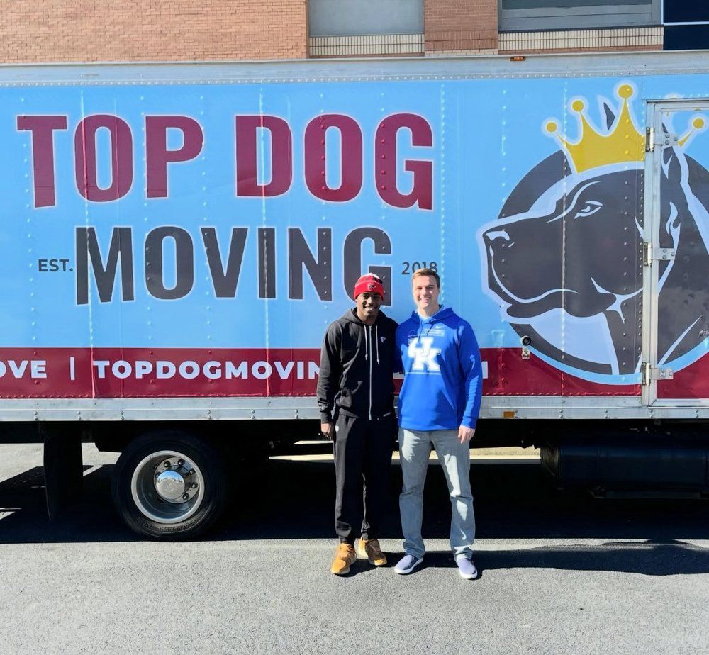 Two men are standing in front of a top dog moving truck
