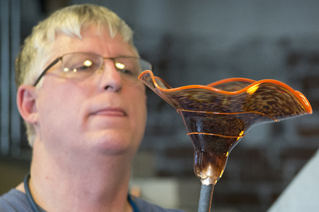 A man wearing glasses is looking at a glass object.