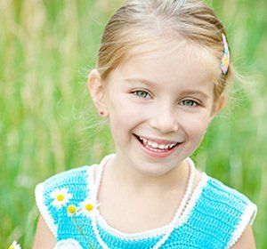 A little girl in a blue dress is holding flowers and smiling.