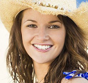 A woman wearing a cowboy hat and a bandana is smiling.