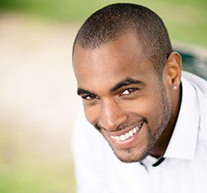 A man in a white shirt is smiling and looking at the camera.