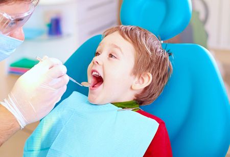 A little boy is sitting in a dental chair getting his teeth examined by a dentist.