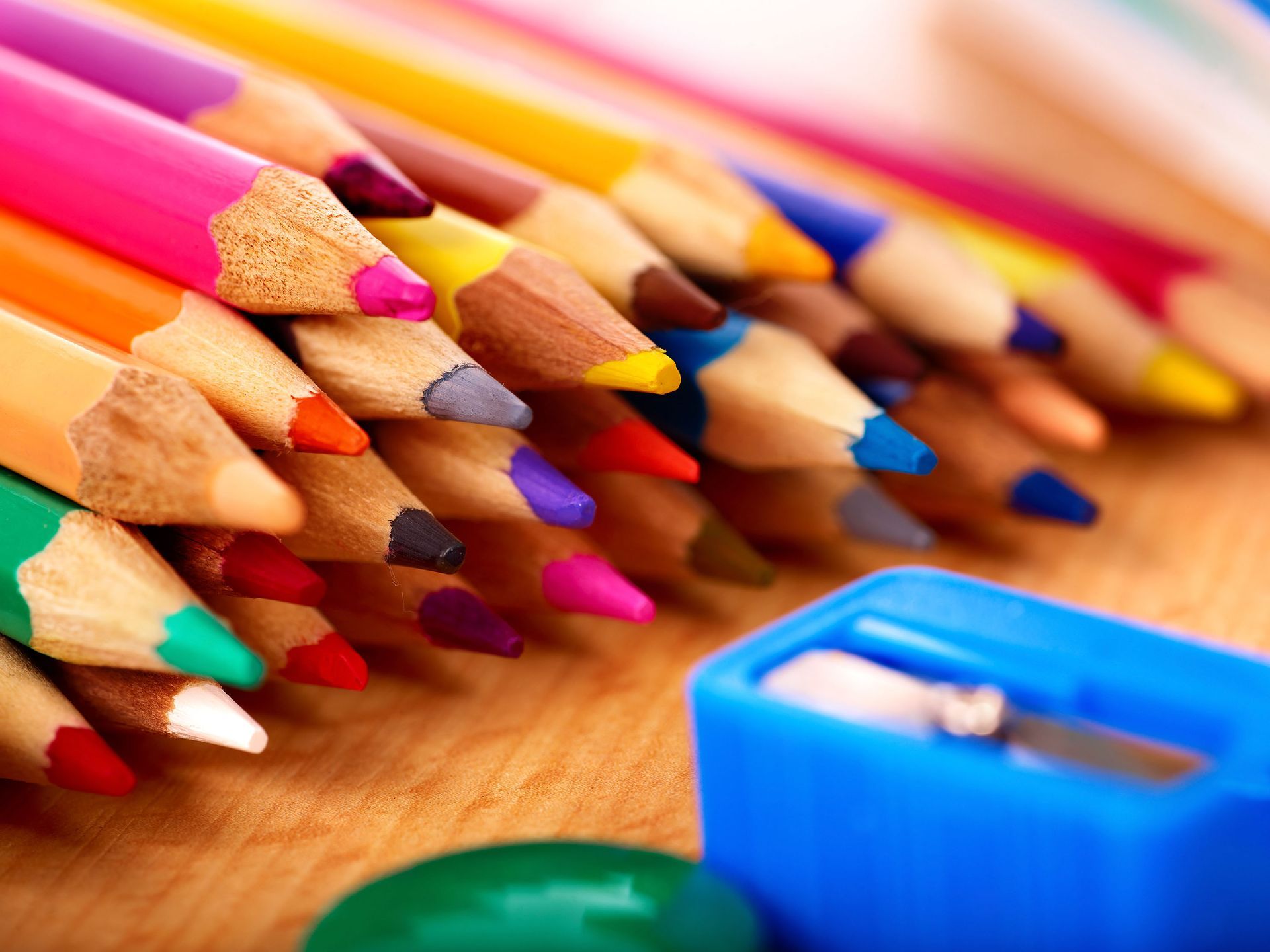 Close-up of colored pencils, various colors, with a blue pencil sharpener on a wooden surface.