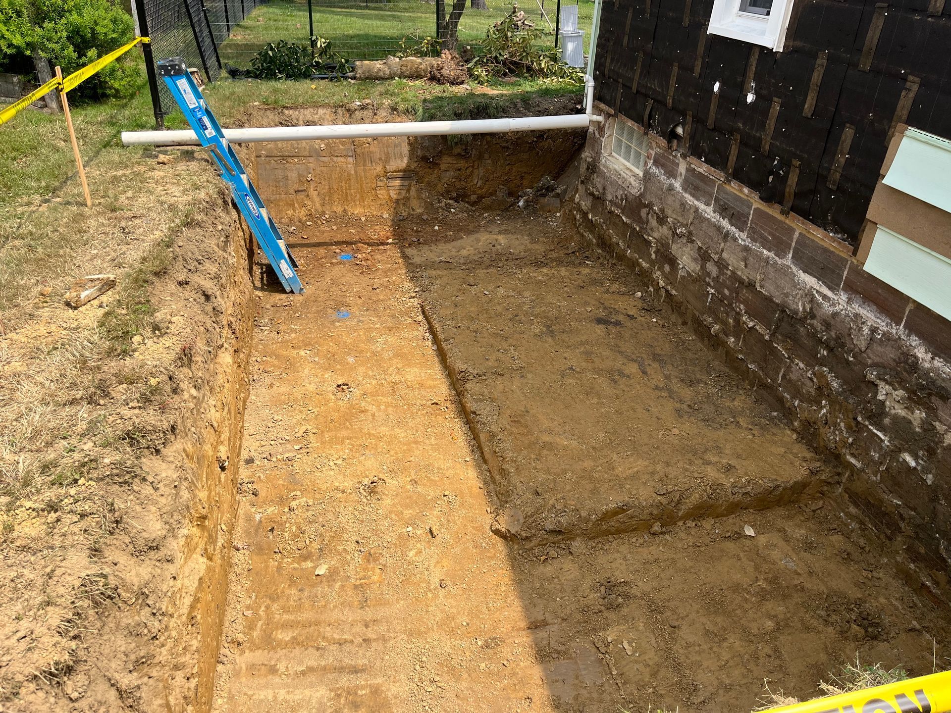 Trench dug next to a house foundation for construction. A level leans against the wall.