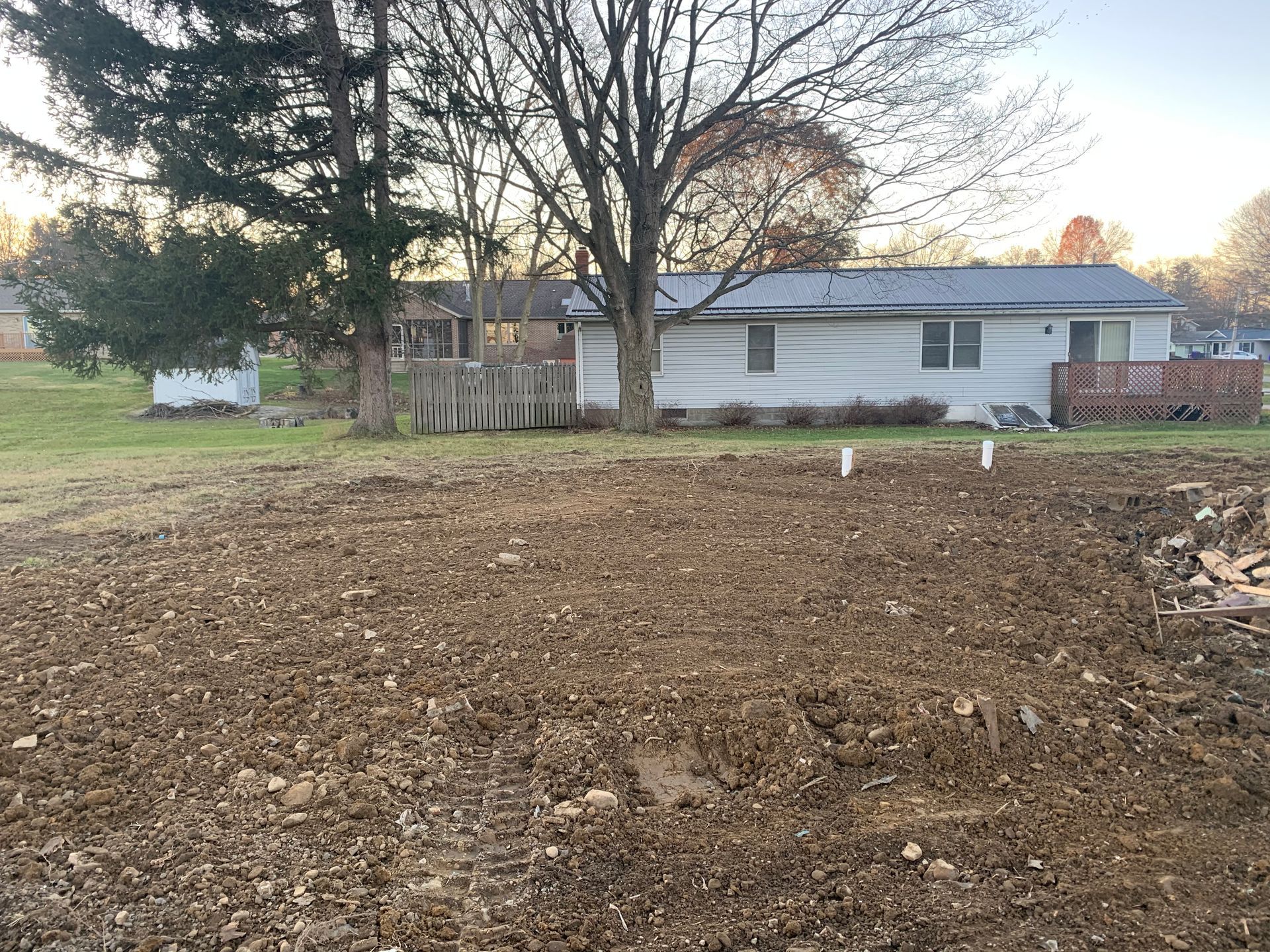 A brown yard in front of a white house with three white pipes in the yard.